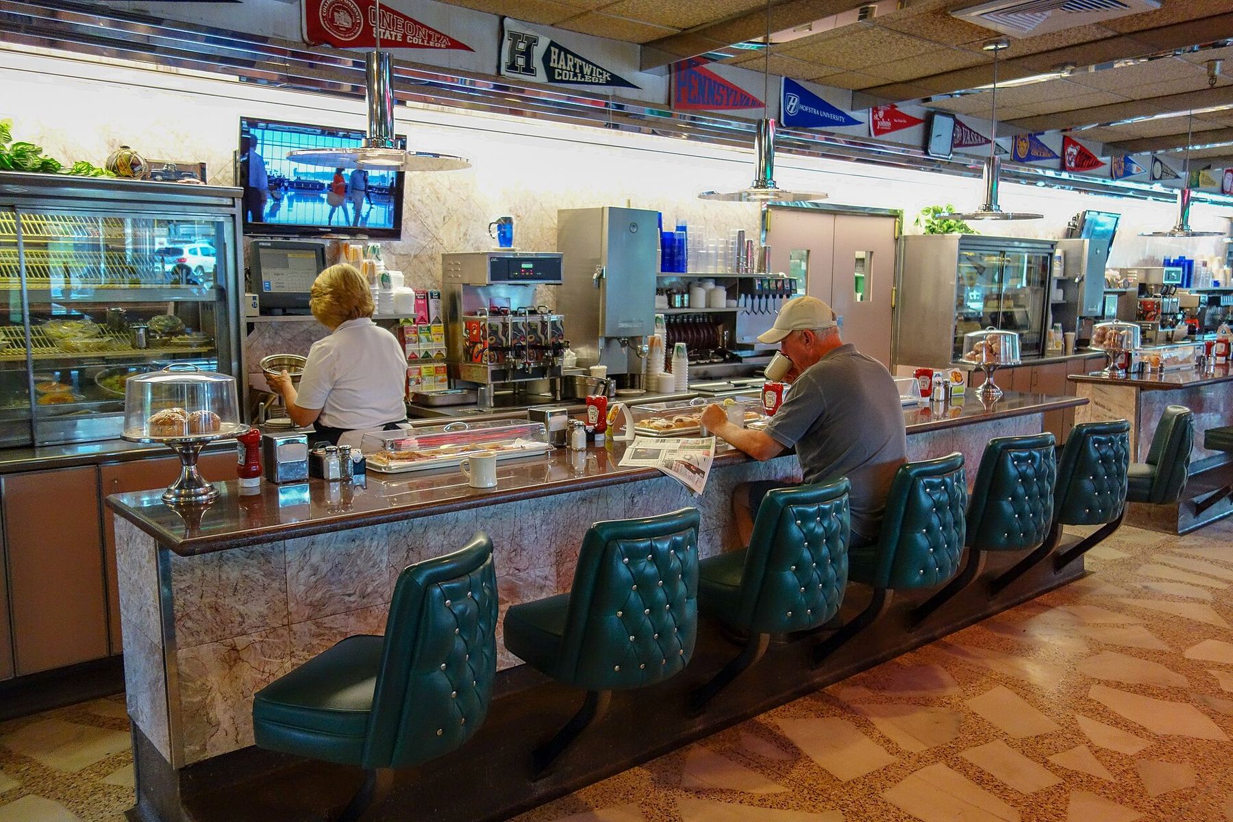A diner counter with green stools and a pie case